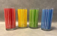 Front view of four retro striped glass tumblers in red, yellow, green, and blue standing upright against a neutral background.