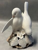 Front view of porcelain love birds figurine showing the pair of birds on a leafy branch base with flowers.