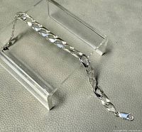 Full view of silver chainlink bracelet with clasp, laid out straight on textured surface with display stands to highlight links detail.