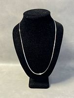 Front view of the necklace displayed on black velvet stand showing flat, shiny chain length.