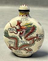 Front side of round Chinese snuff bottle with hand painted orange-red dragon with green and yellow details.