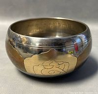 Side view of a round metallic singing bowl with golden lotus petal designs on the outer surface and light scratches.