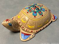 Side angle view of the wooden turtle carving showing the painted central face motif and detailed shell decorations.