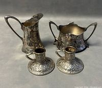 Front view of the set showing the creamer, sugar bowl, and two candleholders with detailed embossed designs.