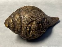 Close-up front and side view of solid brass shankh conch shell showing embossed figure and details
