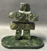Front view of the vintage Inuit Inuk stone sculpture on a light background, highlighting the balanced stacked stone construction and green tonal variations.