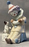 Porcelain clown figurine playing an accordion with a small dog on a die, showing detailed features and colors.