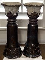 Front view of the two vintage distressed hand painted concrete/cement pedestal votive candleholders showing black paint and raised leaf motifs.