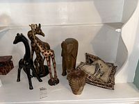 Full view of group including black ceramic giraffe, wood giraffe, carved wood elephant, mini African drum, and fabric placemats with animal motifs.