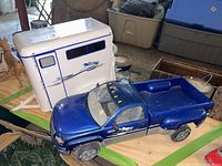 Blue toy pickup truck with open bed, Breyer horse graphic on door, located on wooden surface with storage bins in background
