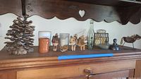 Wide view of assorted items on wooden shelf: large pinecone, candles, wooden animal figurines, glass jars, vintage bottle, and small decorative bird.