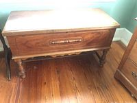 Full view of the wooden cedar chest showcasing its rectangular shape, turned legs, and casters on a wooden floor.