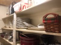 Shelves with stacks of white ceramic dinner plates, dessert plates, and bowls next to a woven basket with a plaid fabric lining.