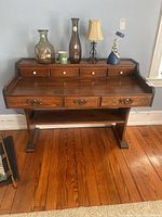 Front view of the vintage wood desk with seven drawers, porcelain and bronze tone pulls, and objects on top.