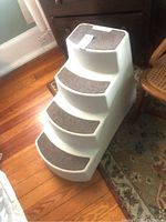 Front and side view of white plastic dog stairs with four carpeted steps placed on wooden floor.
