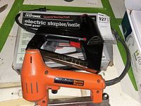 Photo of both electric staplers together showing the black Craftsman stapler with red accents on top and the orange Black & Decker stapler below, cords visible