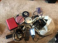 Group of electronics and accessories on carpet including two portable CD players, flip phone, cords, and other small devices.