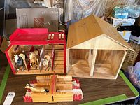 Wooden horse stalls and toy horses placed on table along with wooden trailer parts in a basement setting