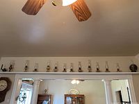Wide view showing the full set of 14 vintage hurricane lamps displayed above a doorway, arranged in a line. One lamp has a dark circular backplate, different from the others.