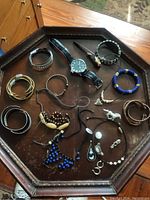 Full overview of the jewelry lot with bracelets, necklaces, earrings, and Minnie Mouse watch arranged on an octagonal wooden tray