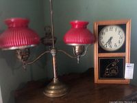 Lamp and clock shown together on a wooden surface against a green wall background