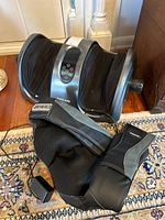 Photo of both massagers together on a floor showing the Tisscare foot massager with dual foot slots and the Maxcare leg shiatsu massager lying on the floor.