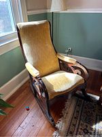 Front and right side view of a Lincoln-style rocking chair with heavy dark wood frame and beige upholstery. The chair shows wear consistent with use and a pet-friendly home.
