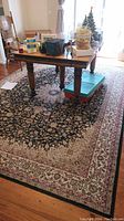 Full view of the area rug under a wooden dining table with chairs showing the floral patterned border and dark central field.