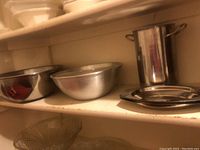Four stainless steel bowls and other kitchenware items on shelf