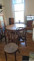 Photo showing the round wooden dining table fully set up with 5 matching chairs around it, seated on wood flooring in front of a window