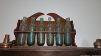 Full view of six vintage glass bottles held in a wooden bottle holder mounted on the wall.