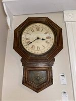 Full view of octagonal wooden wall clock with lower compartment and faux pendulum behind glass.