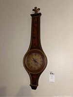 Full view of long vintage wooden wall clock with carved floral inlays and circular clock face with Roman numerals.