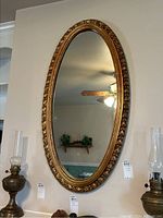 Full view of the oval gold framed wall mirror hanging on the wall, showing its size and shape.