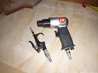 Pair of air tool attachments viewed from above on wooden surface, featuring Chicago Pneumatic air impact wrench with black grip and air blow gun nozzle with chrome and black trigger handle.
