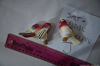 Pair of ceramic bird salt and pepper shakers lying down with visible cork stoppers and ruler for scale.