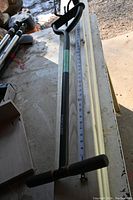 Full length view of the Fiskars long-handled tiller showing the steel shaft and D-shaped handle grip with a measuring tape alongside indicating length.