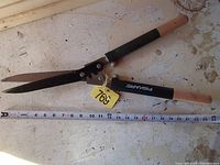 Full view of the Fiskars hedge shears showing wooden handles and blade length next to measuring tape.