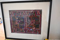 Framed embroidery art showing full piece with glass reflection and black frame.