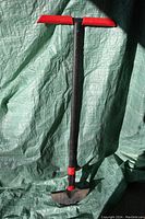 Full view of the Garant turf edger showing black metal handle with red grips and serrated metal blade resting against a tarp.