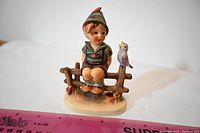 Front view of the Goebel figurine showing the boy sitting on a fence with bird and ruler for scale.
