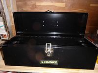 Black shiny metal toolbox with the lid open, showing the empty interior and the Husky brand label on the front.