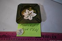 Top view showing Moorcroft ashtray with floral design and attached authenticity tag, yellow sticky note with label, ruler for size reference.