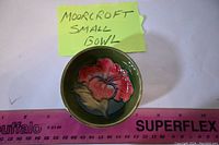 Top view showing the detailed red flower painted inside the small green bowl with a ruler for scale.