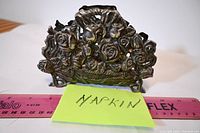 Front view showing detailed floral and rose design napkin holder on a ruler for size reference.