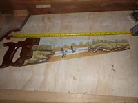 Full length view of the hand saw showing the painted blade with ducks, water, and landscape.