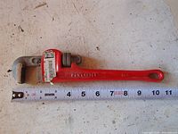 Full view of red 10 inch Power Fist pipe wrench alongside a ruler showing length.