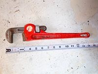 Full length view of a red Mastercraft pipe wrench beside a measuring tape showing approximately 14 inches in length.