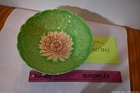 Top view showing green bowl with embossed leaves outside and large flower inside, placed next to a ruler for size reference