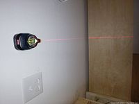 Laser level mounted on wall projecting red laser line horizontally to adjacent surface